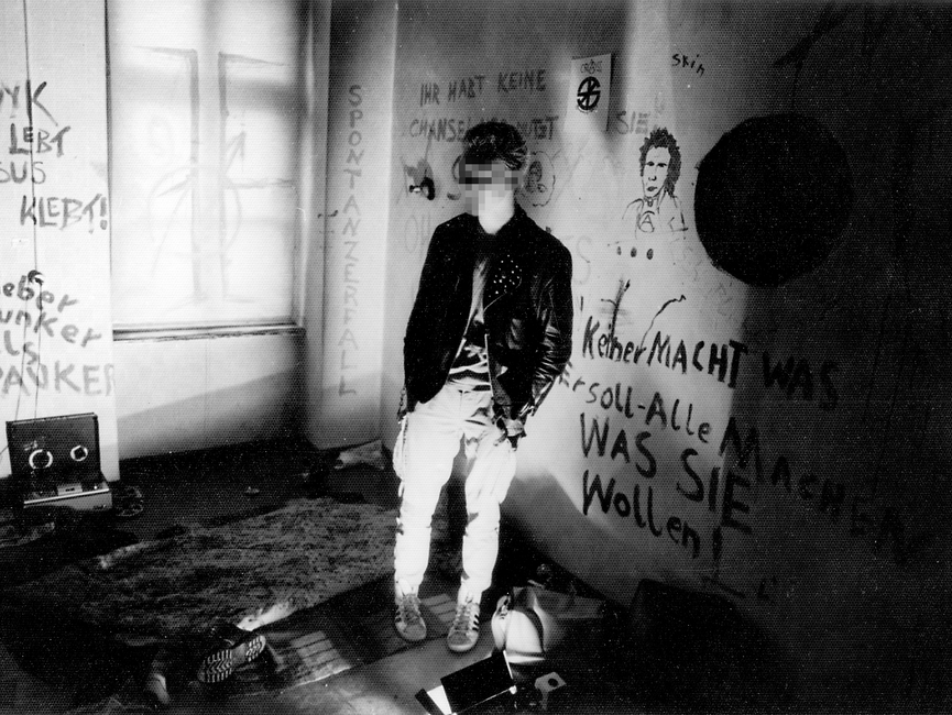 Aufnahme von einem Punk in einem besetzten Haus. Die Wände sind mit Sprüchen bemalt.