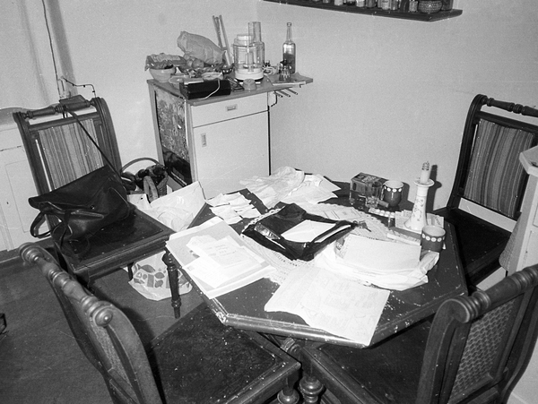 Die Stasi fotografierte bei Wohnungsdurchsuchungen Zimmer so, wie sie sie vorfand. Zu sehen ist ein Tisch mit vier Stühlen. Auf dem Tisch liegen viele Blätterstapel durcheinander.