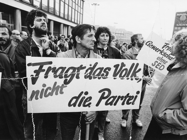 Auf dem Schwarz-Weiß-Bild sind mehrere Demonstrantinnen und Demonstranten zu sehen. Einer von Ihnen hält ein Transparent mit der Aufschrift "Fragt das Volk, nicht die Partei".