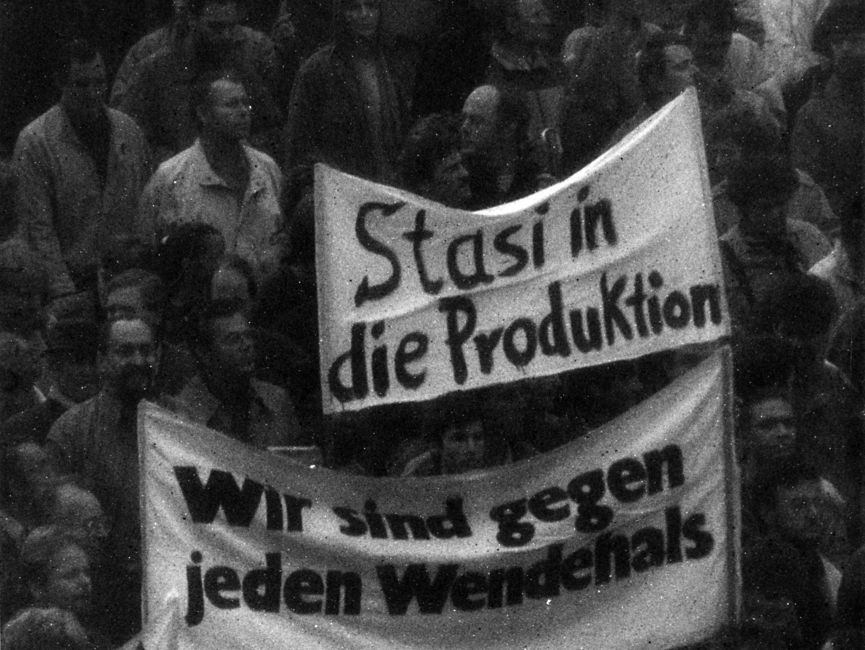 Blick auf Demonstration: Im Mittelpunkt des Bildes stehen zwei Transparente. Auf einem Transparent steht 'Stasi in die Produktion', auf dem anderen 'Wir sind gegen jeden Wendehals'.