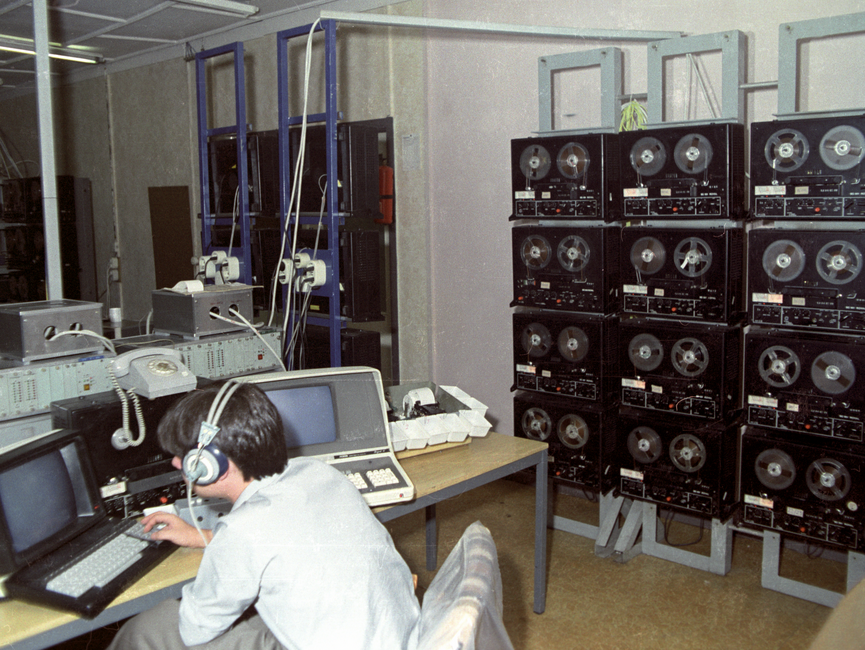 MfS-Mitarbeiter in einem Raum voller Technik zum Abhören und Aufzeichnen von Telefongesprächen.