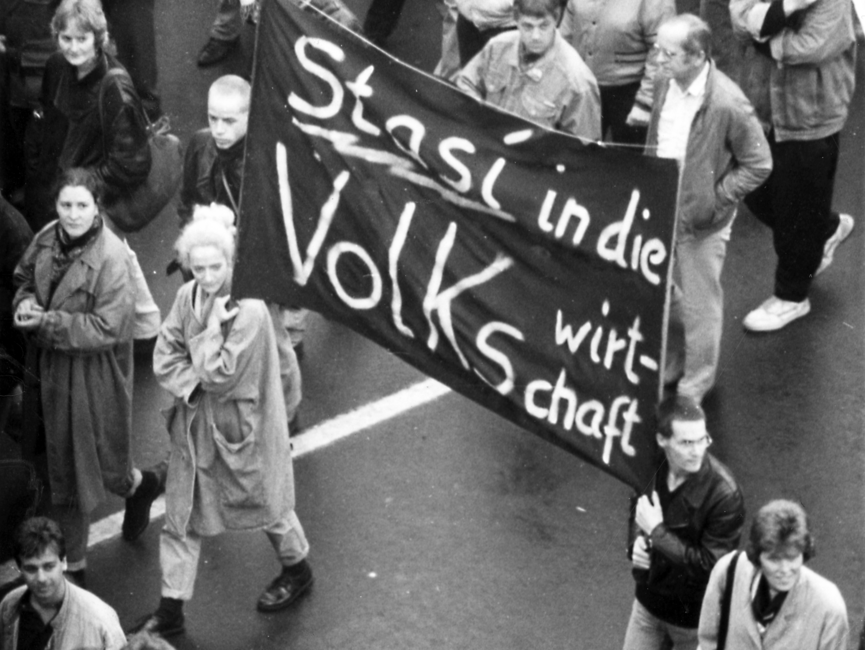 Eine junge Frau und ein junger Mann tragen inmitten einer Demonstration ein Transparent mit der Aufschrift 'Stasi in die Volkswirtschaft'.