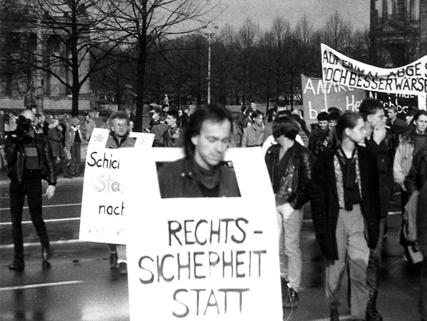 Demonstranten mit Transparenten und Plakaten. Vorne im Bild trägt ein Mann ein Transparent, worauf der Anfang des Schriftzuges 'Rechtssicherheit statt' lesbar ist.