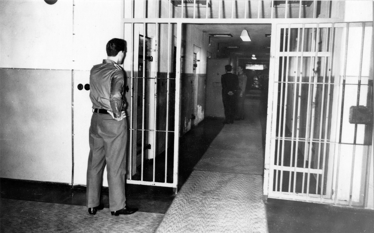 Ein Häftling wird gerade von einem Wärter in seine Zelle gelassen. Ein weiterer Wärter beobachtet das Geschehen. Fotodokumentation der Stasi über Einrichtung und Sicherungsmaßnahmen in Haftanstalten aus dem Jahr 1967. 