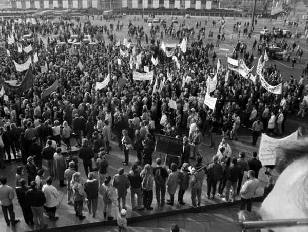 Foto von einer erhöhten Position auf den Alexanderplatz in Berlin, der mit demonstrierenden Menschen gefüllt ist. Aus der Masse ragen mehrere Transparente hervor, die aber nicht zu entziffern sind.