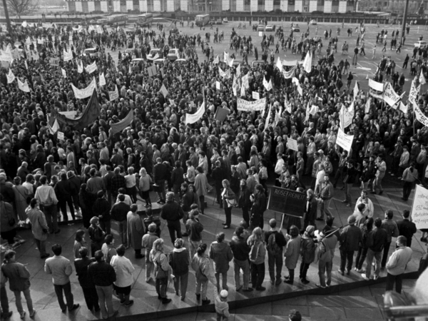 Foto von einer erhöhten Position aus auf den Alexanderplatz in Berlin, der mit demonstrierenden Menschen gefüllt ist. Aus der Masse ragen mehrere Transparente hervor, die aber nicht zu entziffern sind.