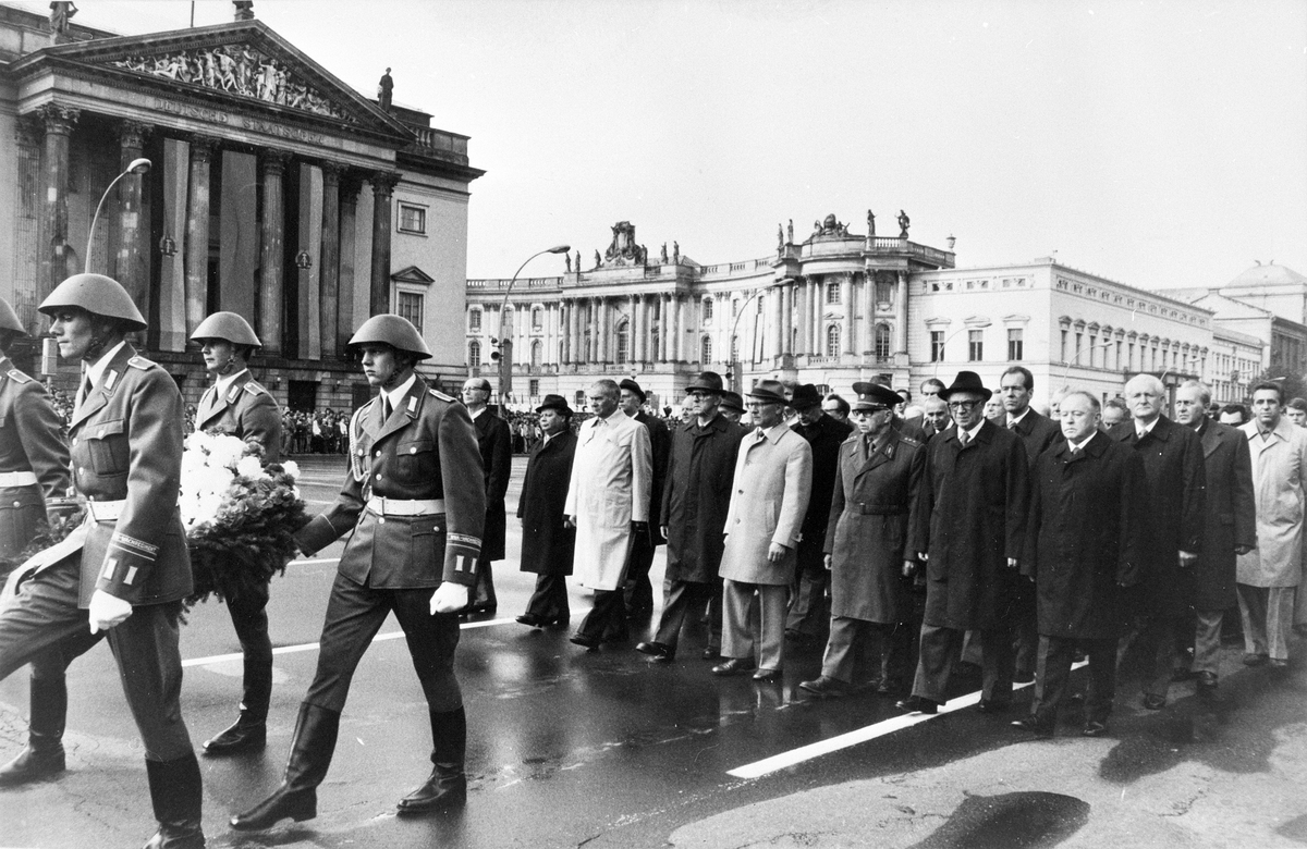 Auf dem Schwarz-Weiß-Bild sieht man den Festumzug angeführt von Soldaten und der SED-Spitze um Generalsekretär Erich Honecker auf der Höhe der Neuen Wache in Berlin-Mitte.